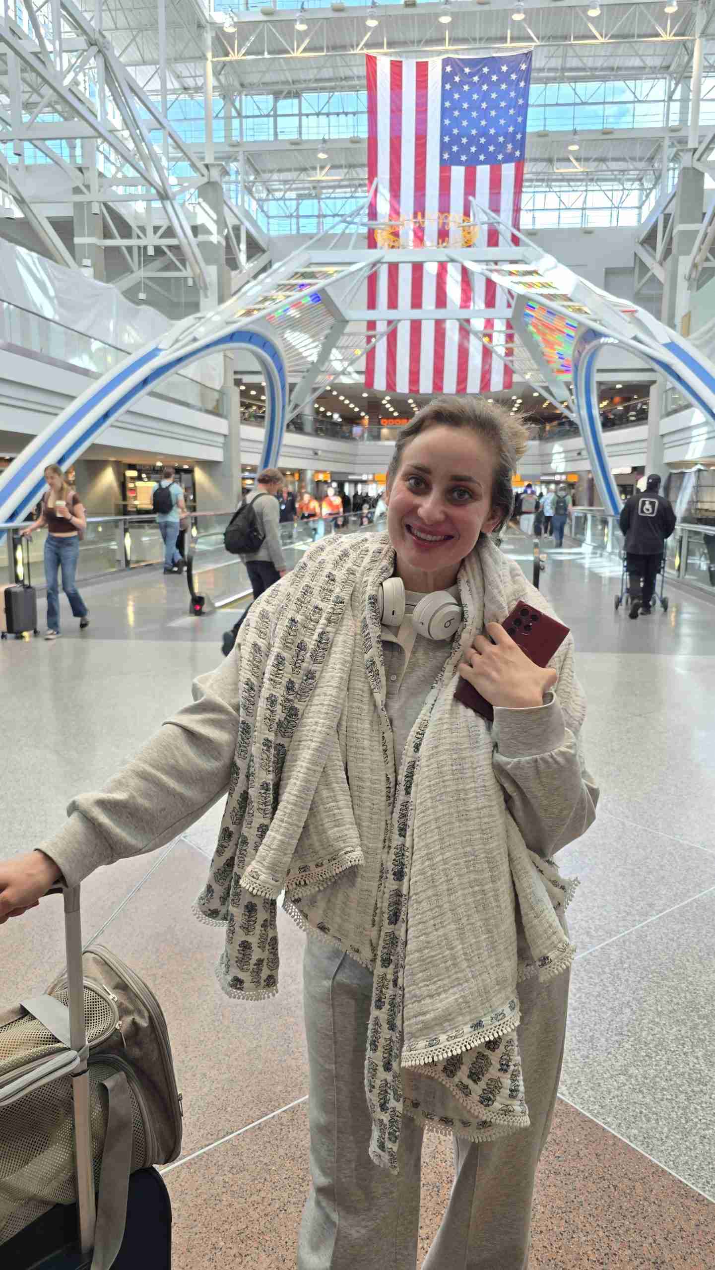 Felicia from Happy Doodle Farm stands with her hand on a carry-on bag and a puppy after arriving at Denver International Airport