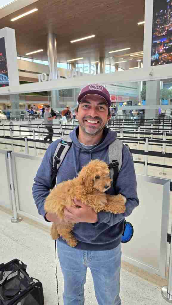 Happy Doodle Farm client from Denver Colorado holds a Cockapoo puppy outside of security entrance at BNA airport in Nashville, Tennessee.